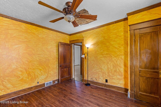 empty room featuring dark wood-type flooring, a textured ceiling, visible vents, ceiling fan, and ornamental molding