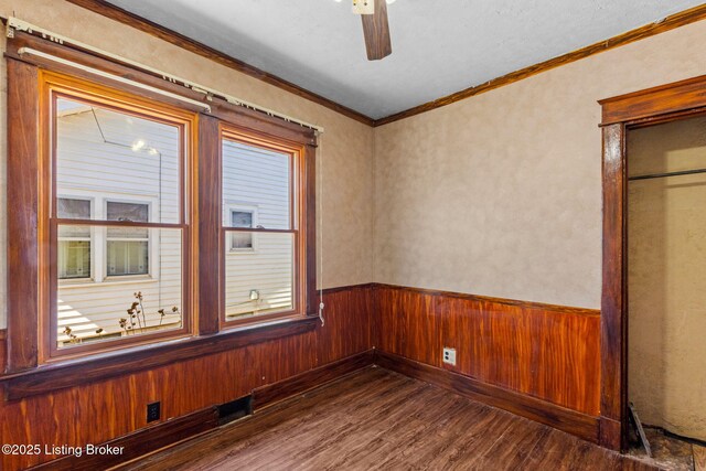 unfurnished room featuring a wainscoted wall, wooden walls, crown molding, ceiling fan, and wood finished floors