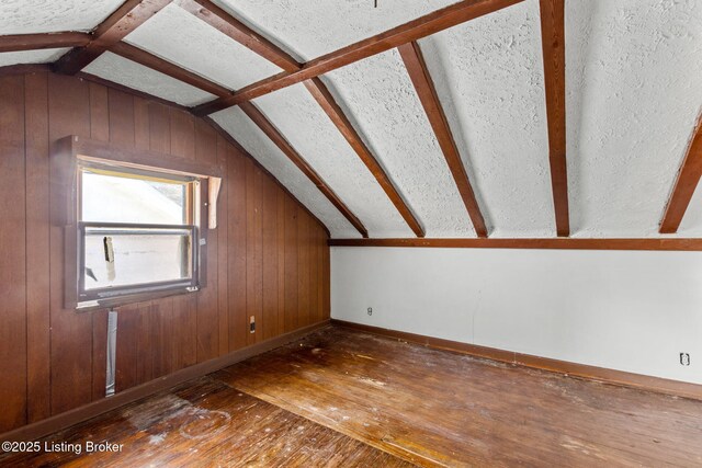 additional living space with hardwood / wood-style floors, baseboards, wooden walls, and vaulted ceiling