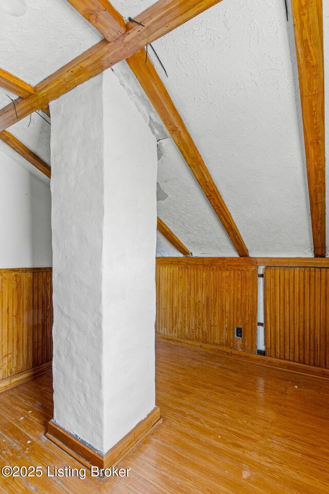 additional living space featuring lofted ceiling with beams, a wainscoted wall, a textured ceiling, wooden walls, and wood finished floors