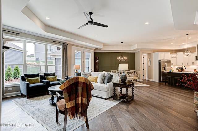 living room featuring baseboards, recessed lighting, a raised ceiling, dark wood finished floors, and ceiling fan with notable chandelier