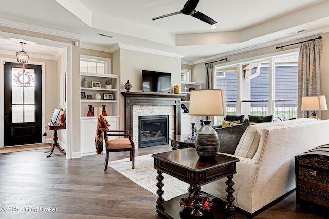 living room with a wealth of natural light, visible vents, a stone fireplace, and a raised ceiling