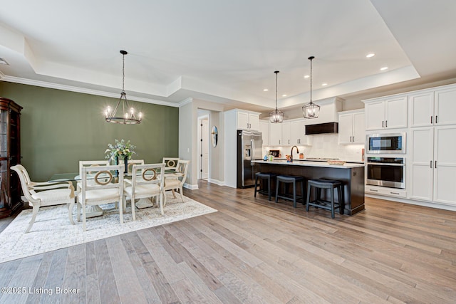 dining space with a raised ceiling, light wood-type flooring, a notable chandelier, and recessed lighting