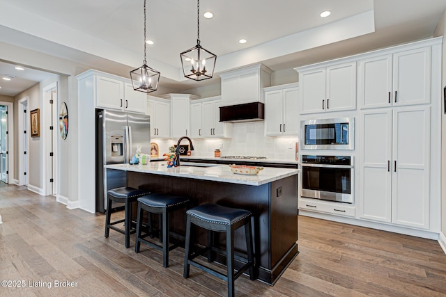 kitchen with a sink, appliances with stainless steel finishes, a kitchen bar, white cabinetry, and backsplash