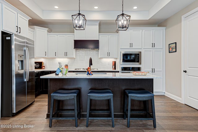 kitchen featuring white cabinets, stainless steel fridge, black microwave, backsplash, and a breakfast bar area