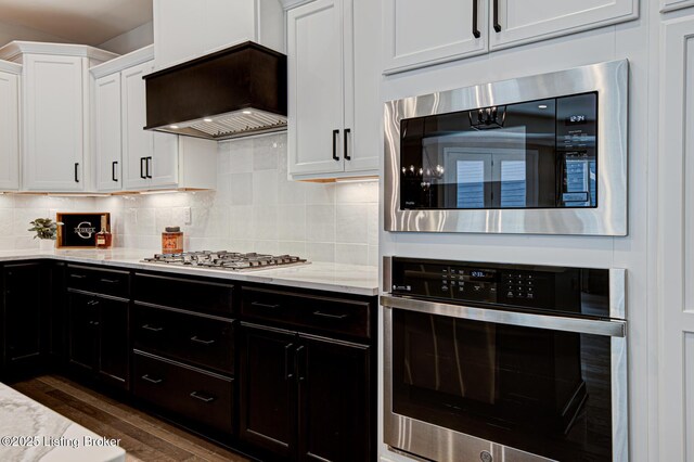 kitchen with custom range hood, light stone counters, dark wood-style floors, white cabinetry, and stainless steel appliances