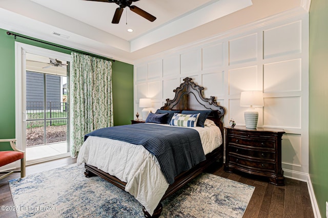 bedroom featuring a decorative wall, access to exterior, a raised ceiling, and wood finished floors