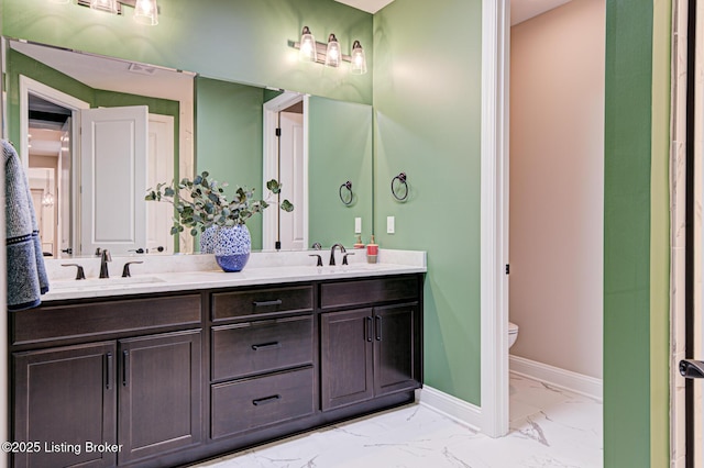bathroom featuring baseboards, double vanity, toilet, marble finish floor, and a sink
