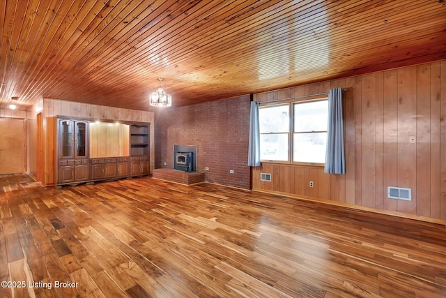 1109 Holly Ave, Louisville, KY 40118 - unfurnished living room featuring light wood-style floors, wood ceiling, wooden walls, a wood stove, and a chandelier