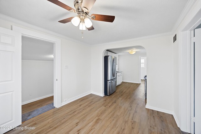 interior space with a ceiling fan, wood finished floors, arched walkways, and ornamental molding