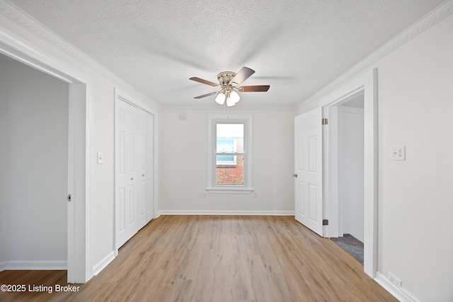 unfurnished bedroom featuring a textured ceiling, light wood finished floors, baseboards, and ornamental molding