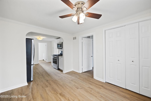 unfurnished living room featuring light wood finished floors, arched walkways, visible vents, ceiling fan, and ornamental molding