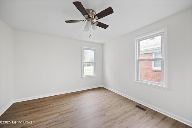 spare room with wood finished floors, visible vents, a ceiling fan, and baseboards