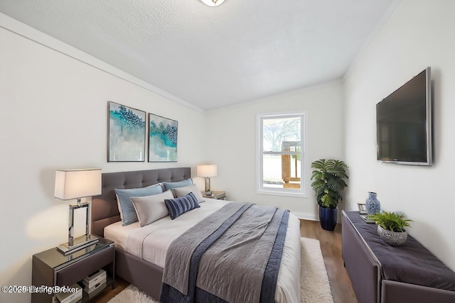bedroom featuring wood finished floors, lofted ceiling, and ornamental molding