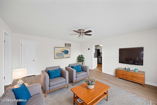 living room featuring light wood-style flooring, a ceiling fan, and baseboards