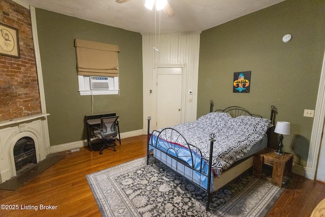 bedroom featuring cooling unit, wood finished floors, a large fireplace, baseboards, and ceiling fan