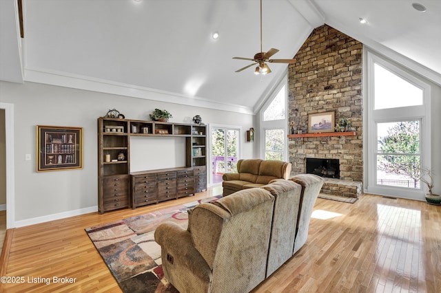 living area with light wood-style flooring, a ceiling fan, a stone fireplace, beamed ceiling, and baseboards