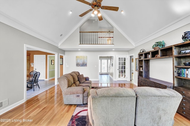 living area with high vaulted ceiling, ceiling fan, light wood finished floors, and baseboards