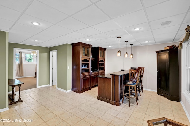kitchen featuring dark countertops, recessed lighting, a kitchen bar, glass insert cabinets, and baseboards