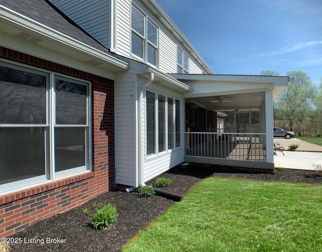 view of side of home with a lawn, brick siding, and a ceiling fan