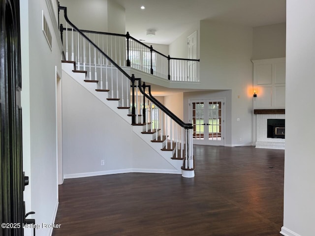 stairway featuring wood finished floors, baseboards, a high ceiling, french doors, and a brick fireplace