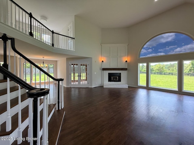 unfurnished living room featuring a chandelier, a towering ceiling, healthy amount of natural light, dark wood finished floors, and baseboards