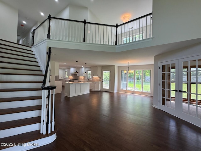 unfurnished living room with dark wood-type flooring, french doors, recessed lighting, a towering ceiling, and a chandelier