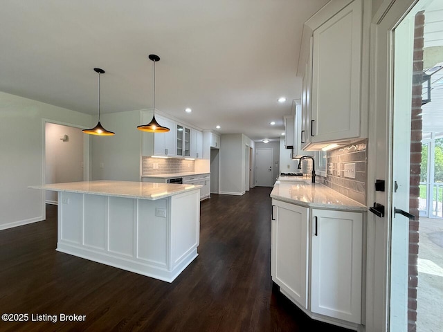 kitchen featuring baseboards, dark wood finished floors, backsplash, white cabinetry, and a sink