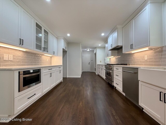 kitchen with stainless steel appliances, glass insert cabinets, dark wood-type flooring, white cabinets, and recessed lighting