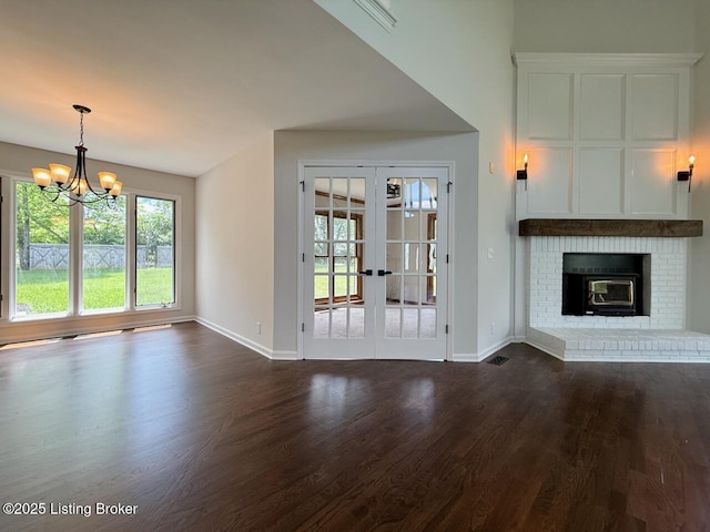 unfurnished living room with dark wood-style floors, a chandelier, baseboards, french doors, and a brick fireplace