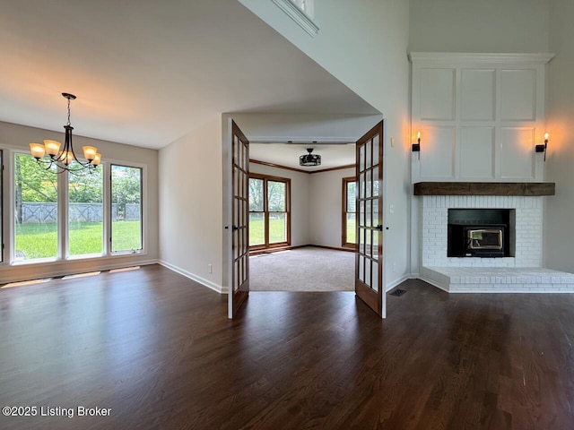 unfurnished living room with a chandelier, baseboards, french doors, dark wood-style flooring, and a brick fireplace
