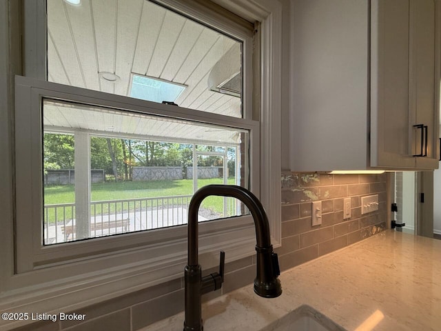 kitchen view of decorative backsplash, a sink, and light stone counters