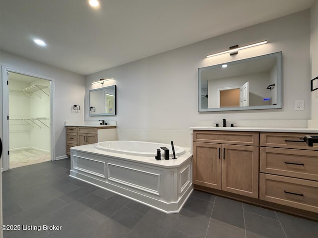bathroom featuring tile patterned floors, a garden tub, recessed lighting, two vanities, and a walk in closet