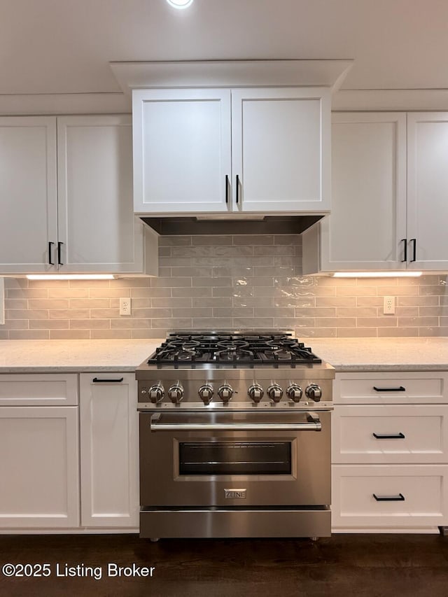 kitchen with high end stove, white cabinetry, light stone counters, and tasteful backsplash