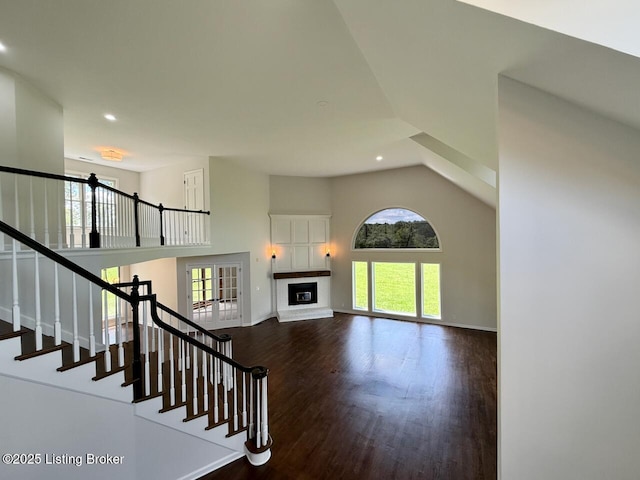 stairway featuring recessed lighting, wood finished floors, a towering ceiling, a glass covered fireplace, and baseboards