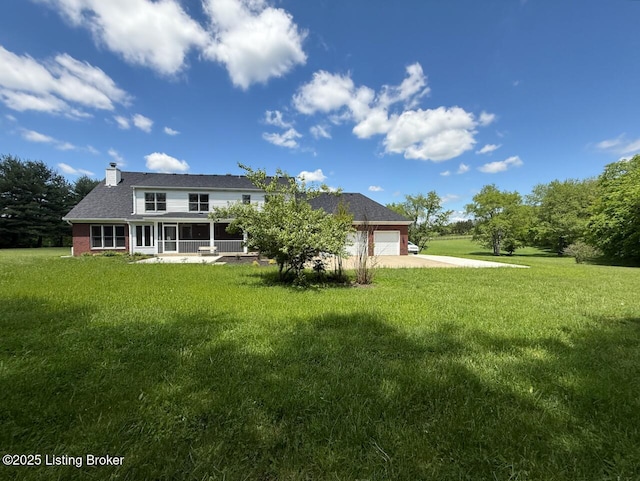 rear view of property featuring concrete driveway, a chimney, a sunroom, a garage, and a yard