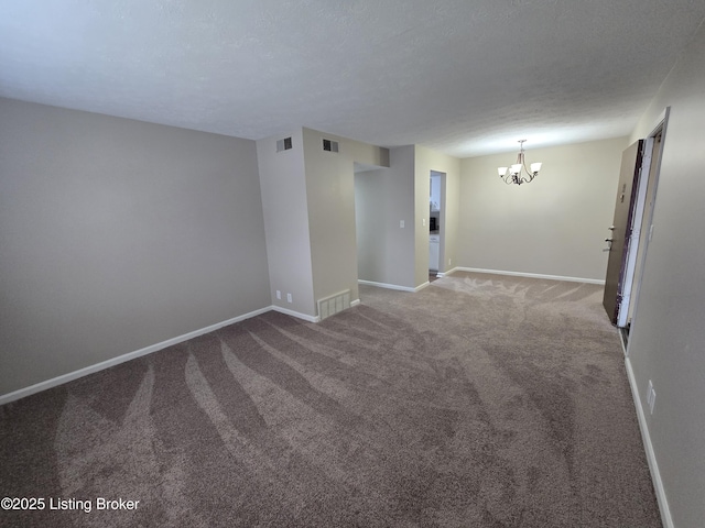 carpeted spare room featuring a textured ceiling, visible vents, baseboards, and a chandelier