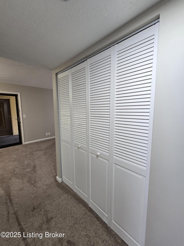 hall featuring baseboards, dark carpet, and a textured ceiling