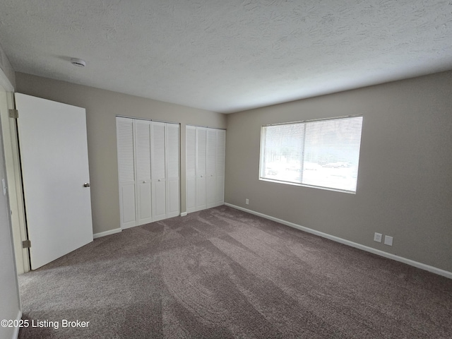 unfurnished bedroom featuring carpet, baseboards, multiple closets, and a textured ceiling