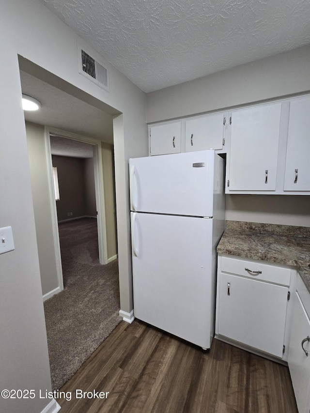 kitchen with freestanding refrigerator, a textured ceiling, dark wood-style floors, visible vents, and white cabinets