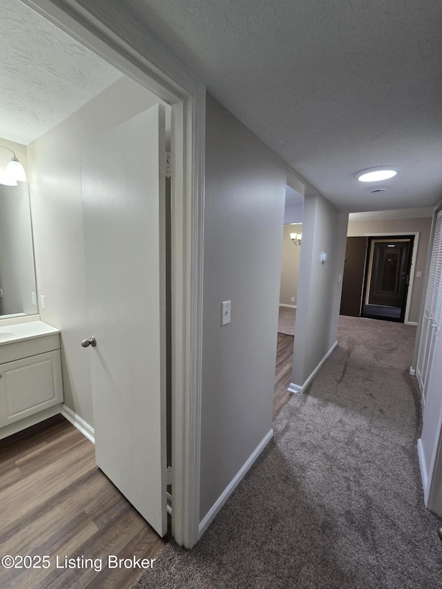 hall with baseboards, wood finished floors, a sink, and a textured ceiling