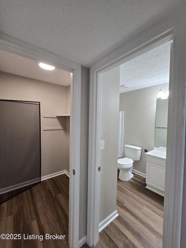 bathroom featuring a textured ceiling, baseboards, toilet, wood finished floors, and vanity