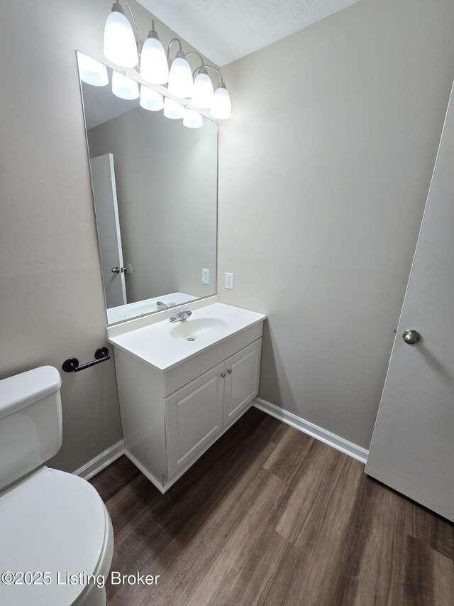 bathroom featuring baseboards, wood finished floors, toilet, and vanity