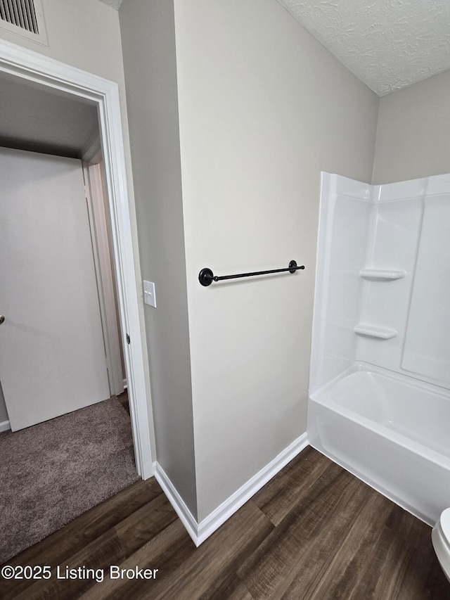 full bathroom with wood finished floors, a textured ceiling, baseboards, and visible vents