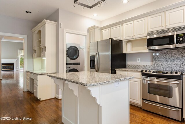 7808 Grenoble Ln, Prospect, KY 40059 - kitchen with stainless steel appliances, stacked washer / dryer, wood finished floors, light stone countertops, and a center island