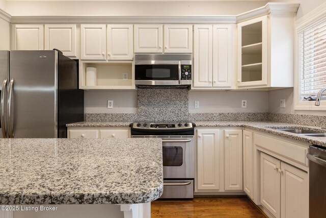 7808 Grenoble Ln, Prospect, KY 40059 - kitchen featuring appliances with stainless steel finishes, a sink, glass insert cabinets, light stone counters, and wood finished floors