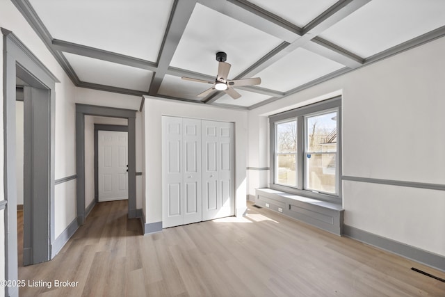 unfurnished bedroom featuring a closet, baseboards, beam ceiling, light wood-style floors, and coffered ceiling