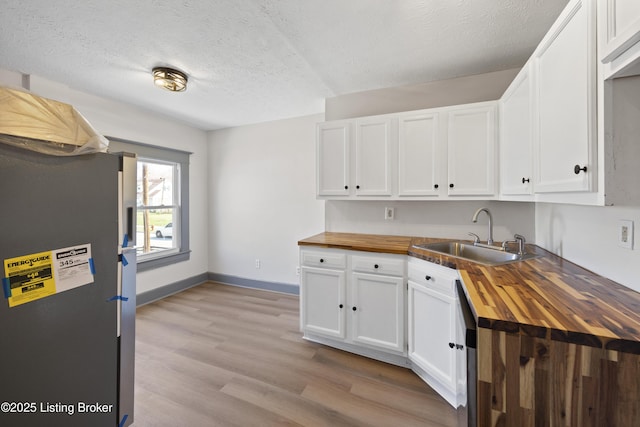 kitchen featuring a sink, freestanding refrigerator, white cabinetry, wooden counters, and light wood-style flooring