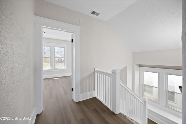 corridor featuring an upstairs landing, lofted ceiling, dark wood-style flooring, baseboards, and visible vents