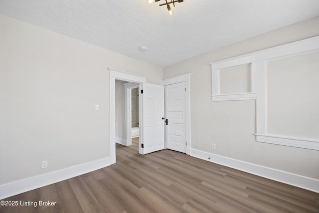 spare room featuring baseboards, wood finished floors, and a textured ceiling